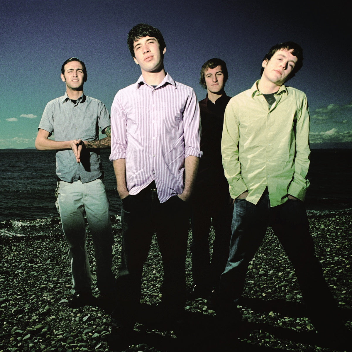 Four men standing on a rocky beach with the ocean and sky in the background.